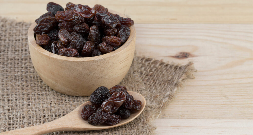 A wooden bowl filled with raisins.