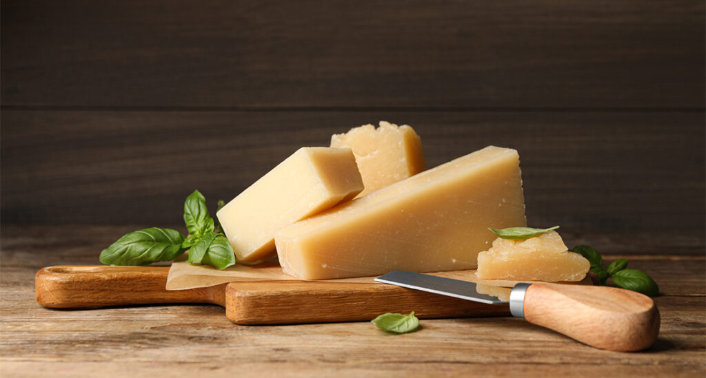 A wooden cutting board with cheese and basil leaves.