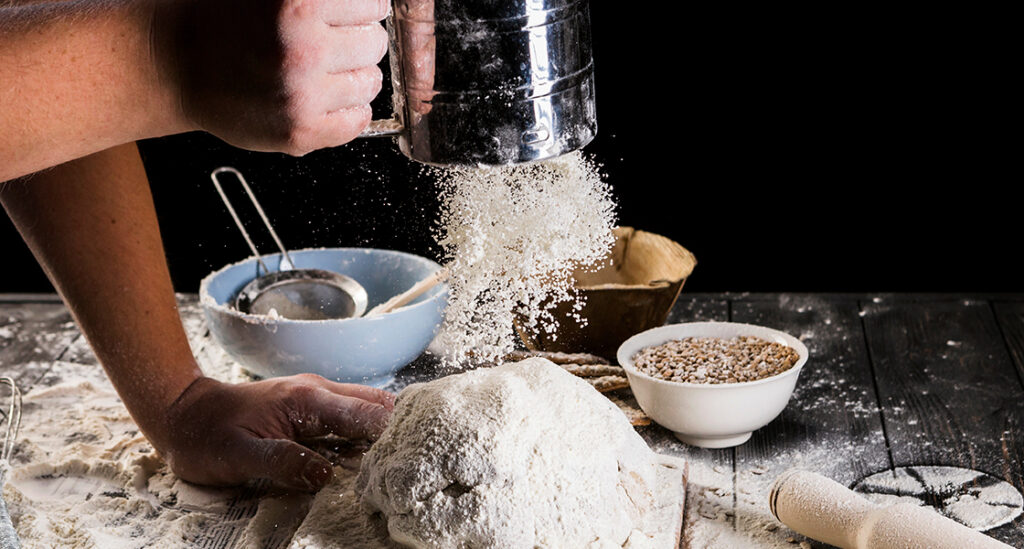 A baker sprinkling flour over bread dough